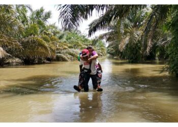 MUSTAPA Muhamaddin mendukung isterinya meredah banjir di Kampung Selat Manggis, Sungai Kerawai, Teluk Intan di sini semalam.-UTUSAN/ AIN SAFRE BIDIN