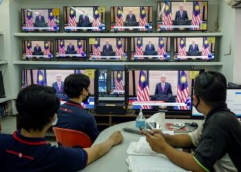 PEKERJA di sebuah kedai  barangan elektrik di Kuala Lumpur mendengar ucapan Perdana Menteri yang disiarkan di televisyen dan media sosial seluruh negara, semalam.– UTUSAN/FARIZ RUSADIO