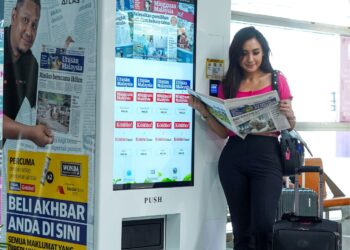 Pramugari, Zulaikha Ariffin, 28, membaca Utusan Malaysia yang dibeli dari mesin layan diri sementara menunggu perkhidmatan e-hailing di Stesen Sentral Kuala Lumpur, semalam. – UTUSAN/MUHAMAD IQBAL ROSLI