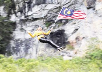 SEORANG pengunjung sedang melakukan aktiviti zipline sambil memegang Jalur Gemilang di pusat rekreasi Via Ferrata Kota Gelanggi di Jerantut, Pahang. - UTUSAN/HARIS FADILAH AHMAD