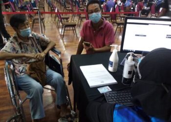 YEW Moy (kiri, berkerusi roda) ditemani menantunya, Siew Tong (kanan) ketika sesi pendaftaran bagi menerima vaksin Covid-19 di PPV Mega UiTM Puncak Alam, Kuala Selangor, Selangor hari ini. - UTUSAN / MOHAMAD NAUFAL MOHAMAD IDRIS