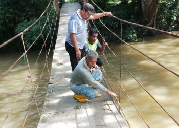 Mohd. Sabri Ahmad (duduk, hadapan) dan Mohd. Ehsan Abdullah (duduk, belakang) menunjukkan besi kabel yang menahan lantai besi jambatan gantung yang longgar di Kampung Paya, Pulai, Baling hari ini.- UTUSAN/ZAID MOHD NOOR