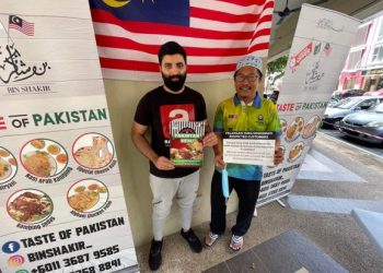 FAISOL Munjir (kiri) dan rakan niaganya, Mohd. Arham menunjukkan notis makanan percuma dan menu di hadapan restoran itu di Setia Alam, semalam. – UTUSAN/ISKANDAR SHAH MOHAMED.