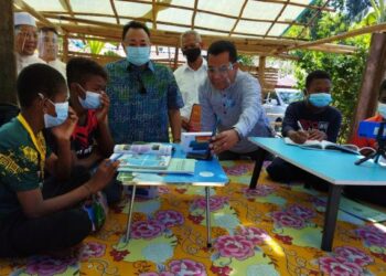 AMMAR Shaikh Mahmood Naim (berdiri, tengah) melihat anak-anak Orang Asli  belajar secara dalam talian selepas majlis penyerahan bantuan telefon pintar kepada Orang Asli di Perkampungan Orang Asli, Lubuk Legong, Kampung Lalang, Baling hari ini.