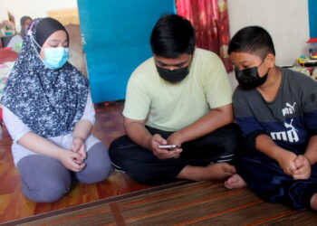 Irfan Izzuddin Zaharuddin (tengah) bersama dua adiknya, Iffah Damiah (kiri) dan Isyarah Muizzuddin berkongsi telefon bimbit yang diberikan percuma untuk mengikuti PdPR di Kampung Sungai Chengeh, Serkat Pontian di sini semalam.  -UTUSAN/MUHAMMAD ZIKRI