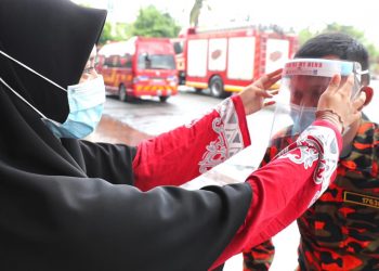 PELAJAR SMK Munshi Abdullah, Hanin Fadhlina Omar, 16 (kiri) memakaikan pelindung muka kepada anggota bomba, Azwan Mohd. Said selepas majlis penyerahan di Balai Bomba dan Penyelamat Ayer Keroh, Melaka. UTUSAN/ RASUL AZLI SAMAD