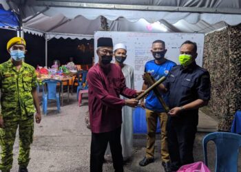 HASAN Rahman menyerahkan lemang kepada salah seorang anggota polis yang bertugas di pos pengawal di pintu masuk Kampung Permatang Tulang, Sebatu, Jasin, Melaka, baru-baru ini. -  UTUSAN/AMRAN MULUP