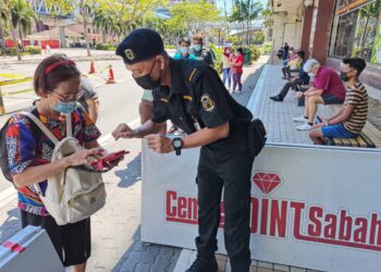 PENGAWAL  keselamatan Centre Point Sabah di Kota Kinabalu memeriksa aplikasi MySejahtera salah seorang pelanggan di pintu masuk utama pusat membeli belah berkenaan.