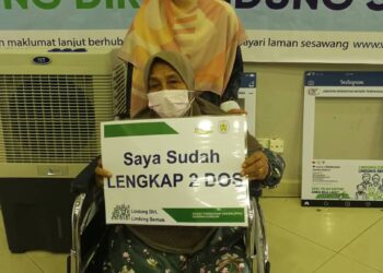 ZAINUN Salleh ditemani cucunya, Aqilah Haziqah Azhan ketika menerima suntikan vaksin di Pusat Pemberian Vaksin (PPV) Politeknik Sultan Mizan Zainal Abidin di Dungun, baru-baru ini. - UTUSAN/NIK NUR IZZATUL HAZWANI NIK ADNAN