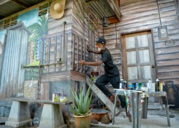 MOHD. Rozamil Mohd. Yatim menyiapkan lukisan mural rumah kampung bagi mengisi masa terluang semasa Perintah Kawalan Pergerakan (PKP) di bengkel miliknya di Chendering, di Kuala Terengganu. - UTUSAN/PUQTRA HAIRRY ROSLI