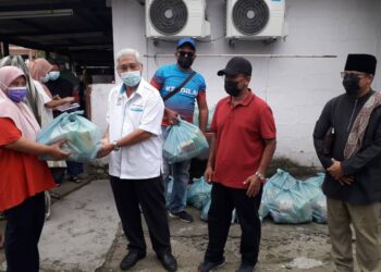 HASSAN Karim (tengah) menyerahkan bantuan barang keperluan asas kepada penduduk di Kampung Pertanian, Pasir Gudang di Johor.