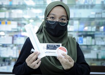PETUGAS farmasi menunjukkan kit Covid-19 Ag Saliva Home Test keluaran SD Biosensors yang dijual di Farmasi V-Care, Putrajaya. - UTUSAN/FAIZ ALIF AHMAD ZUBIR