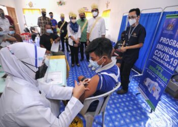 KHAIRY Jamaluddin dan Mohd. Salim (lima dari kanan) melihat seorang warga masyarakat orang Asli menerima vaksin di Pusat Pemberian Vaksin (PPV) Bergerak, Kampung Orang Asli Batu Peti, Jempol. - UTUSAN/MOHD. SHAHJEHAN MAAMIN