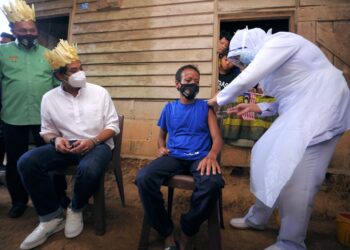 KHAIRY Jamaluddin dan Mohd. Salim Mohd. Sharif (kiri) melihat seorang warga masyarakat orang Asli, Azman Undi, 45, yang menerima vaksin di hadapan rumahnya di Kampung Orang Asli Batu Peti, Jempol. - UTUSAN/MOHD. SHAHJEHAN MAAMIN