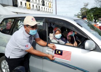 KHAIRUL Shahril Mohamed meletakkan pelekat magnet Jalur Gemilang pada kereta seorang penerima vaksin Covid-19 sempena Program Kempen Kibar Jalur Gemilang Negeri Perak di PPV Stadium Indera Mulia, Ipoh. - UTUSAN/ZULFACHRI ZULKIFLI