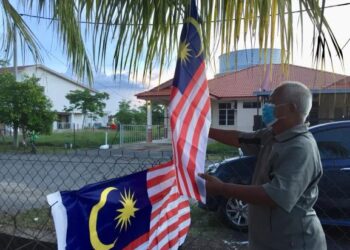 MUSTAFFA Hussain memasang Jalur Gemilang ketika ditemui di rumahnya di Gong Badak di Kuala Nerus, kelmarin. – UTUSAN/TENGKU DANISH BAHRI TENGKU YUSOFF