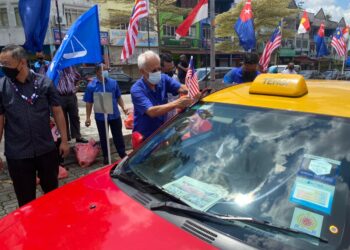 SHAHRIR Samad (kanan) memasang bendera semasa menghadiri program penyerahan 100 bakul makanan dan Jalur Gemilang kepada pemandu teksi di ruang parkir Pejabat UMNO Bahagian Johor Bahru di Johor.