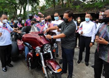 HASNI Mohammad (depan, dua kanan) melekatkan Jalur Gemilang pada salah sebuah motosikal pada Program Penyerahan Jalur Gemilang di Jalan Yahya Awal, Johor Bahru di Johor. -UTUSAN/RAJA JAAFAR ALI