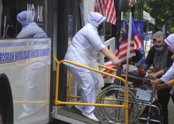 PETUGAS kesihatan membantu seorang penduduk berkerusi roda yang hadir untuk menerima vaksin Covid-19 pada Program Mobilisasi Vaksin Komuniti di Dewan Orang Ramai Taman Siliau Jaya, Siliau, Port Dickson. -UTUSAN/MOHD. SHAHJEHAN MAAMIN