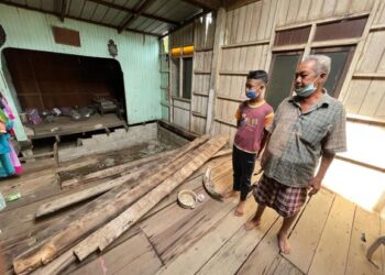 ISMAIL Daud menunjukkan sebahagian lantai papan rumah yang terpaksa dibuang kerana reput di Kampung Danan, Pasir Puteh. - UTUSAN/TOREK SULONG