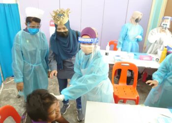 SAPIAH Mohd. Nor (berdiri, dua kiri) membantu menenangkan individu Orang Asli sindrom down yang menerima suntikan vaksin Covid-19 di Kampung Orang Asli Simpang Arang, Iskandar Puteri, di Johor.