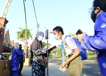 SEORANG pelajar melakukan pemeriksaan suhu sebelum memasuki sekolah Sekolah Menengah Kebangsaan (SMK) Paya Besar di Kuantan, Pahang. - UTUSAN/SHAIKH AHMAD RAZIF