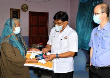 NOR Fairus Johar (kiri) menerima bayaran faedah Perkeso daripada Mohd. Izhar Ahmad sambil diperhatikan Tong Sing Chuang di Flat Serantau, Larkin di Johor. -UTUSAN/RAJA JAAFAR ALI