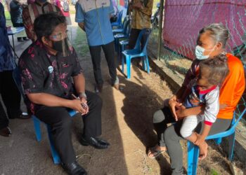 KAMEL Mohamad (kiri) beramah mesra dengan seorang penerima vaksin ketika lawatan program vaksinasi orang asli di Balai Raya Taman Kejora, Kuala Sungga, Melaka. - UTUSAN/DIYANATUL ATIQAH ZAKARYA