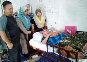 NORHASLINDA Hassan terlantar di katil ditemani oleh suaminya, Kamaruddin Mohd. Kholik (kiri) dan dua orang anak di Felda Tekam Utara di Jerantut, Pahang. – UTUSAN/HARIS FADILAH AHMAD