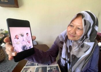 BAGI mengubati kerinduan, Nooren Rashid, melihat gambar anak dan menantunya sebelum mereka pulang ke kampung halaman selepas ini di Taman Guru Jaya, Kangar, Perlis, semalam. – UTUSAN/NAZLINA NADZARI