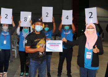 AZWAN Atan (depan, kiri) merupakan penerima dos terakhir yang ke-282,428 diraikan oleh Penyelaras PPV Midvalley Haliza Khalid (kanan) sebelum tamat operasi di PPV Midvalley Southkey di Johor Bahru. - UTUSAN/RAJA JAAFAR ALI