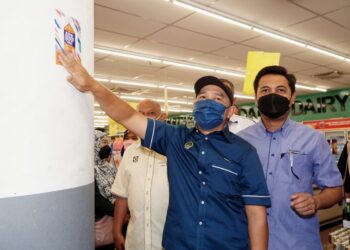 ABDUL Yunus Jamahri menampal pelekat AKHP di CK Supersave Mart di Pulau Pangkor. - UTUSAN/ZULFACHRI ZULKIFLI