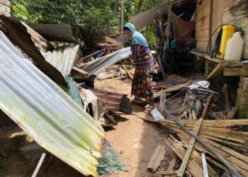 FARIDAH Wahab membersihkan sebahagian zink dan papan dinding bahagian dapur rumahnya yang runtuh dalam kejadian banjir di Kampung Lentang, Belantik, hari ini. - UTUSAN/NORLIA RAMLI