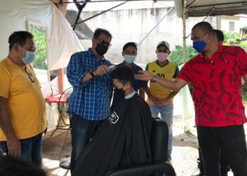 AZAHA Abdul Rani (dua dari kiri) menggunting rambut seorang pelajar di Kampung Cina, Gua Musang, Kelantan, petang semalam. - UTUSAN/AIMUNI TUAN LAH