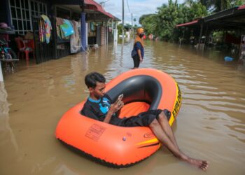 SEORANG mangsa banjir, Muhammad Syarifuddin Ismail bersantai di atas pelampung  di hadapan rumahnya di Taman Tanjung Bendahara, Alor Setar hari ini. - UTUSAN/SHAHIR NOORDIN