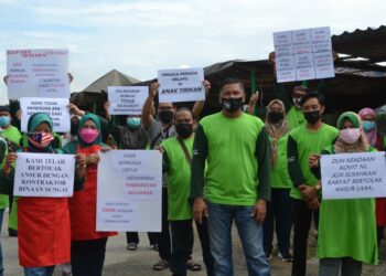 PENIAGA Pekan Sari di Kampung Stesen, Kuala Sawah, Rantau, Seremban memegang sepanduk sebagai tanda protes selepas mereka menerima notis memindahkan gerai daripada pihak MBS. - UTUSAN/ZAKKINA WATI AHMAD TARMIZI