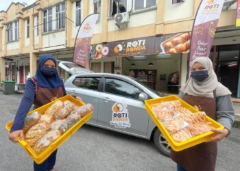 NUR FATIHAH ROSLI (tudung biru) menunjukkan roti yang diletakkan di dalam kereta sebelum dibawa oleh ejen untuk dijual di sekitar negeri ini ketika ditemui di Roti Ronda, Taman Wang Seri, Arau, Perlis baru-baru ini.- UTUSAN/NAZLINA NADZARI