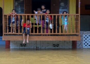 SEKUMPULAN kanak-kanak melihat rumah mereka dinaiki air di Kampung Chalok Kedai di Setiu, hari ini. - UTUSAN/PUQTRA HAIRRY ROSLI