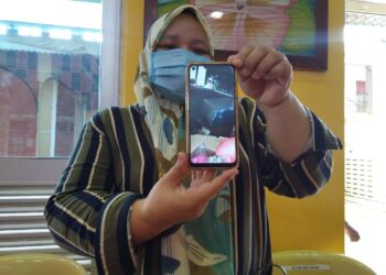 ZURAIDAH Sapine menunjukkan gambar keadaan dalam rumahnya yang musnah selepas dinaiki air banjir. - UTUSAN/MUHAMMAD SHAHIZAM TAZALI