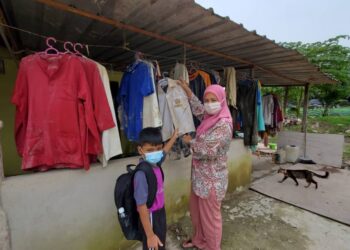ROHANA Mohd. Idris bersama anaknya Muhammad Izzul Danial Mohd. Lapis menunjukkan baju sekolah yang masih terdapat kesan lumpur akibat ditenggelami banjir di rumahnya di Kampung Bukit Lanchong di Shah Alam, Selangor, hari ini.