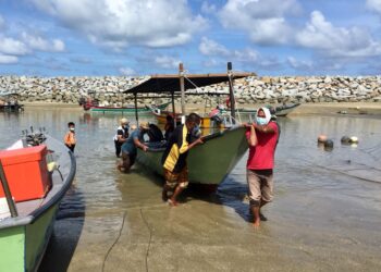 BEBERAPA nelayan terpaksa membantu menaikkan bot rakan mereka susulan masalah muara cetak di Pantai Tok Jembal di Kuala Nerus, semalam. - TENGKU DANISH BAHRI TENGKU YUSOFF