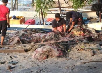 NELAYAN di Kuala Teluk Kumbar, Bayan Lepas, Pulau Pinang bergotong-royong menarik pukat dan menaikkan bot yang terbalik akibat kejadian ribut.