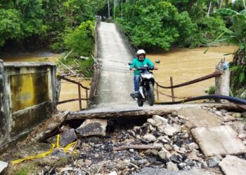 SEORANG penunggang motosikal menggunakan jambatan rosak yang terletak di antara Kampung Padang Cina dan Kampung Landak, Baling. - UTUSAN/NORLIA RAMLI