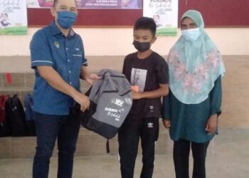 ABDUL Yunus Jamahri (kiri) menyampaikan sumbangan keperluan persekolahan kepada seorang penerima di Tanjung Piandang dekat Parit Buntar semalam. - UTUSAN/WAT KAMAL ABAS