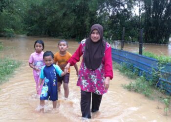 KAMARIAH Ismail memimpin tiga cucunya meredah banjir di Kampung Air Putih di Kemaman hari ini. - UTUSAN/NIK NUR IZZATUL HAZWANI NIK ADNAN