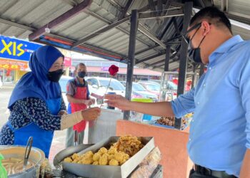 MUHAMAD AKMAL Saleh (kanan) memberikan sekuntum bunga Ros kepada seorang peniaga wanita di Pekan Merlimau, Jasin, Melaka. - UTUSAN/DIYANATUL ATIQAH ZAKARYA