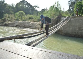 ZATUL Atirah Mohd. Hanafiah meniti batang pokok pinang untuk menyeberang Sungai Temalir di Kampung Temalir, Kuala Krai. – UTUSAN/BAHRUDDIN HATTA