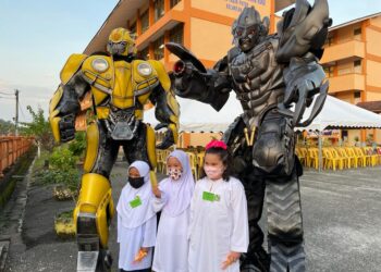 MURID-MURID teruja bergambar dengan Megatron dan Bumblebee pada hari pertama seso persekolahan di SK Cherang Ruku, Pasir Puteh, Kelantan. - UTUSAN/TOREK SULONG