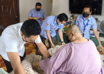 AHMAD Haswadi Hashim (kanan) dan Azmizam Zaman Huri (kiri) sedang membantu Ahmad Shahrul Nizam untuk baring di atas lapik belakang berisi udara di rumahnya di Kampung Nelayan Teluk Gong hari ini. - UTUSAN / ABDUL RAZAK IDRIS