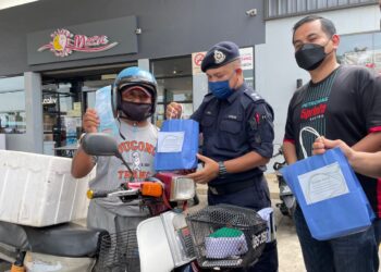 AMRAN@Mohamad Zaki Omar (tengah) menyerahkan sumbangan kepada seorang penunggang motosikal pada Program Jelajah Op Selamat 18 PDRM bersama Petronas di Semabok, Melaka. - UTUSAN/DIYANATUL ATIQAH ZAKARYA